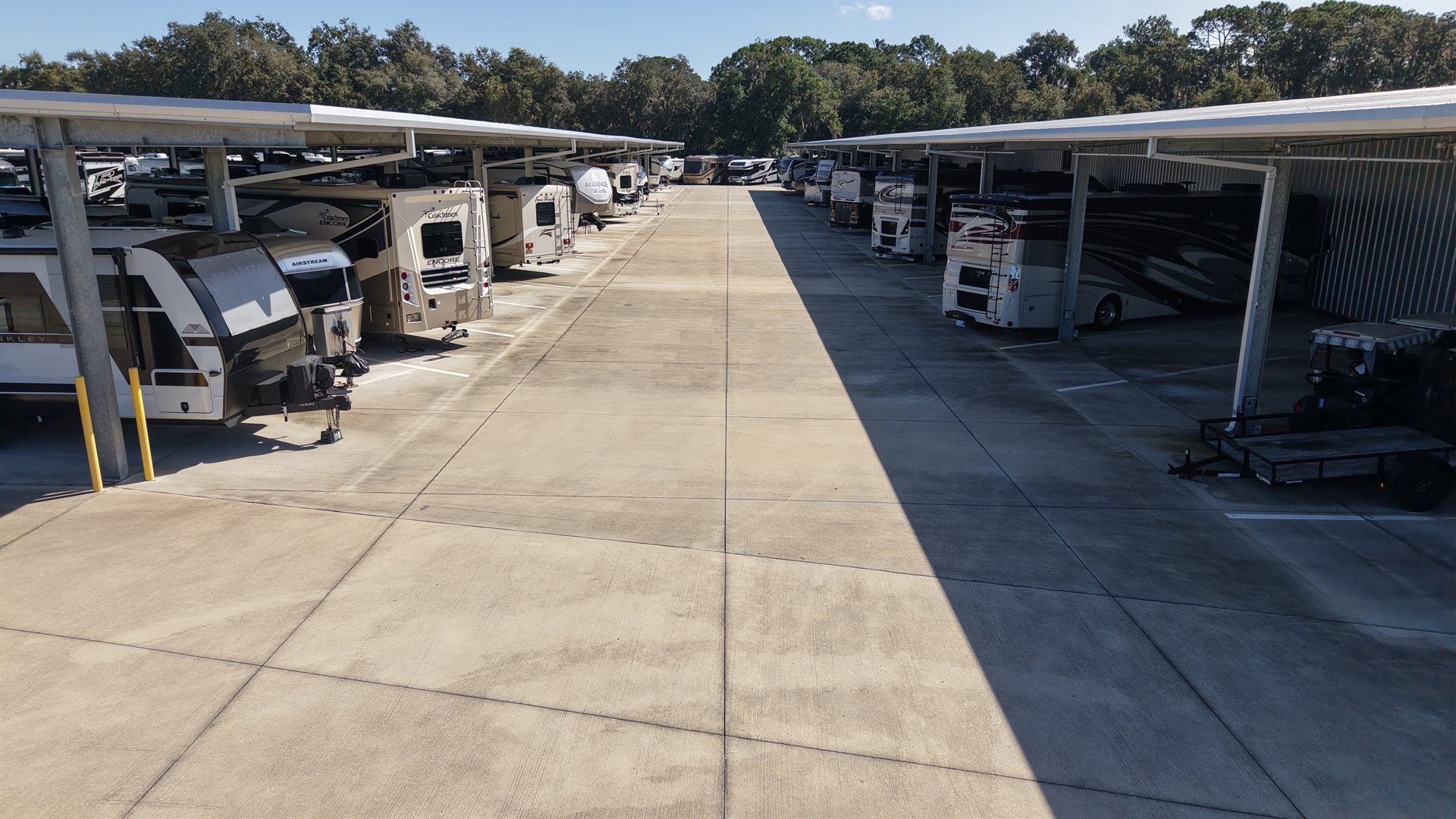Low altitude drone photo of a wide paved drive aisle between covered RV and boat storage canopies
